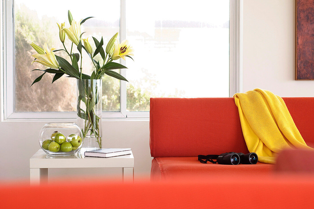 Bouquet of lilies next to an orange designer sofa with yellow throw and telescope