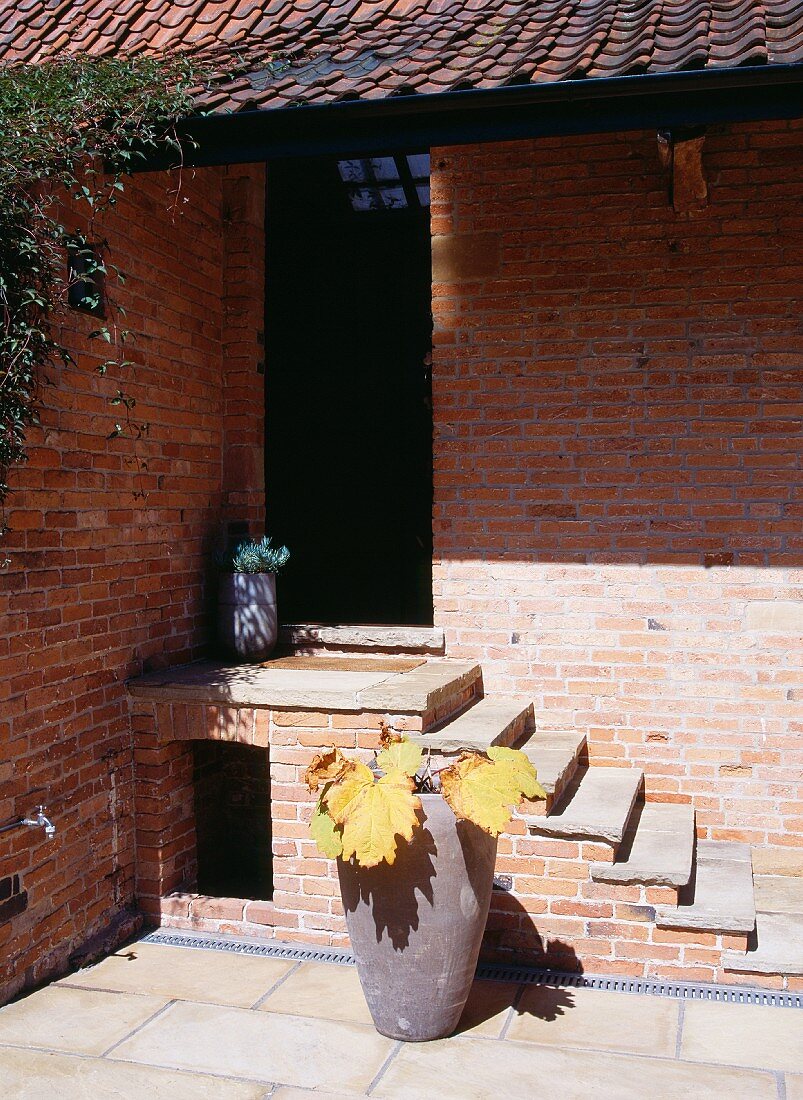 Brick house and entrance steps and ceramic pot with autumn leaves