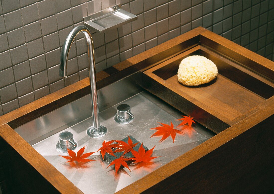 Red autumn leaves lie in minimalist designer sink in wood and stainless steel