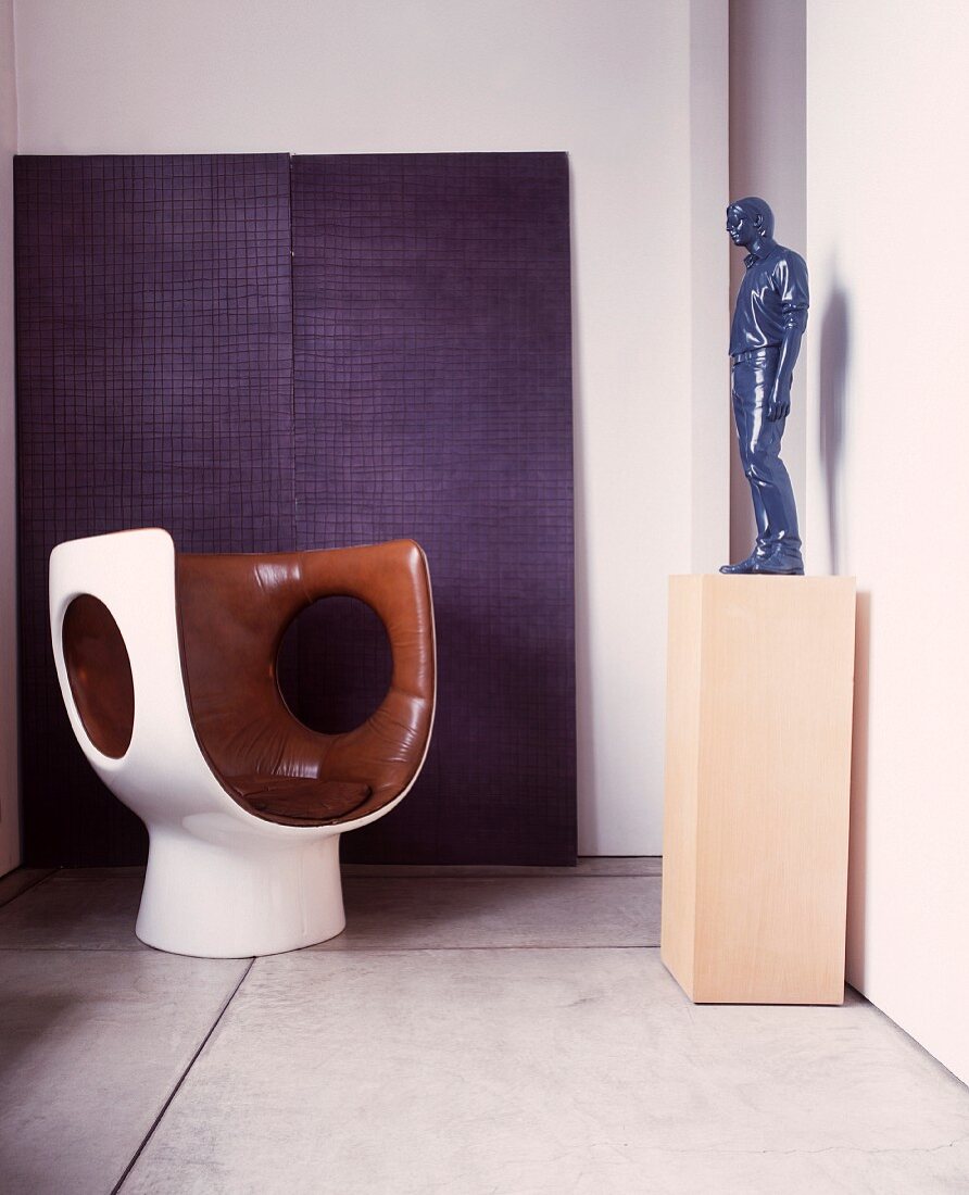 White, plastic shell chair with brown, leather upholstery opposite figure on pedestal