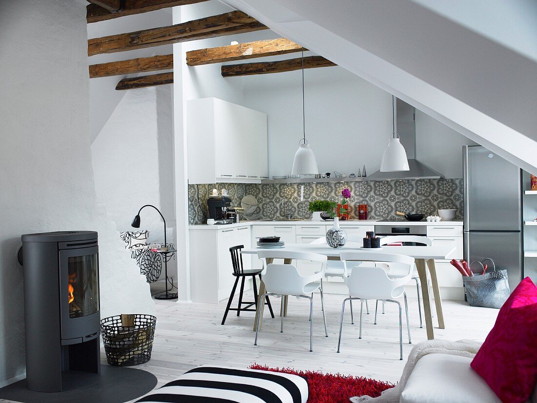 Offener Dachraum mit schlichter Küche, Essplatz und Schwedenofen im jungen, skandinavischen Stil