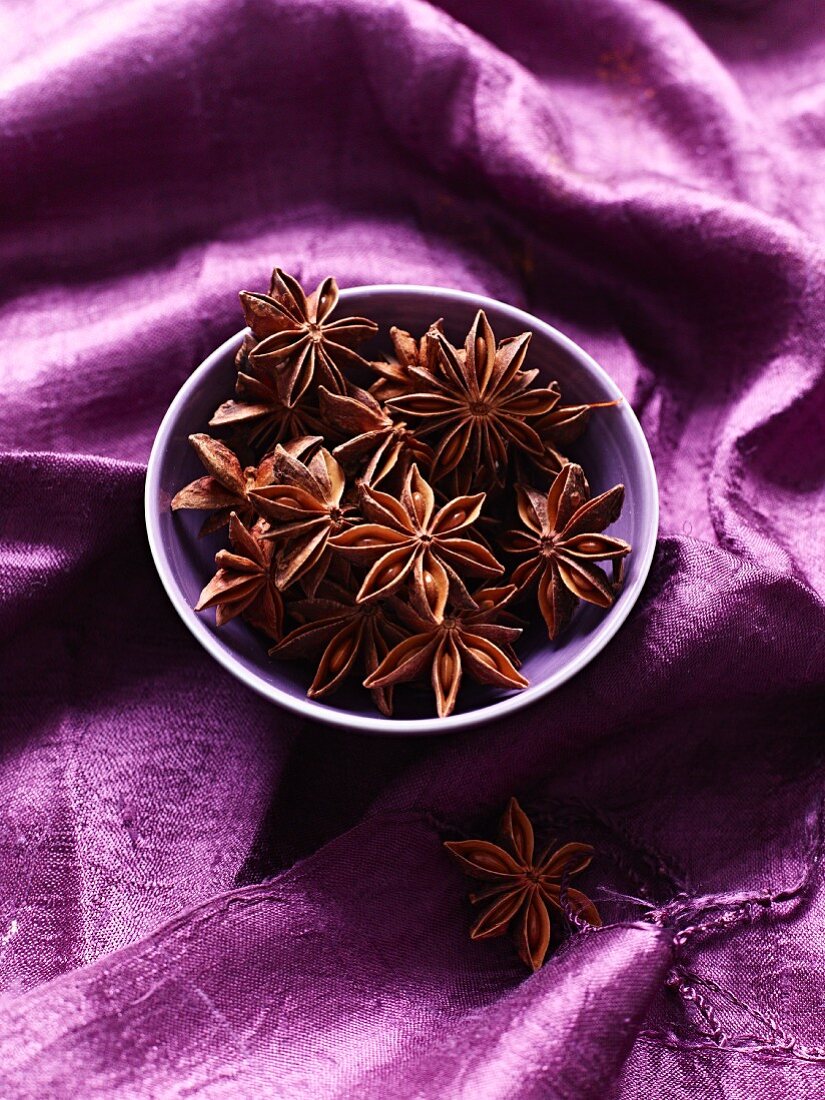 Star anise in bowl on purple cloth
