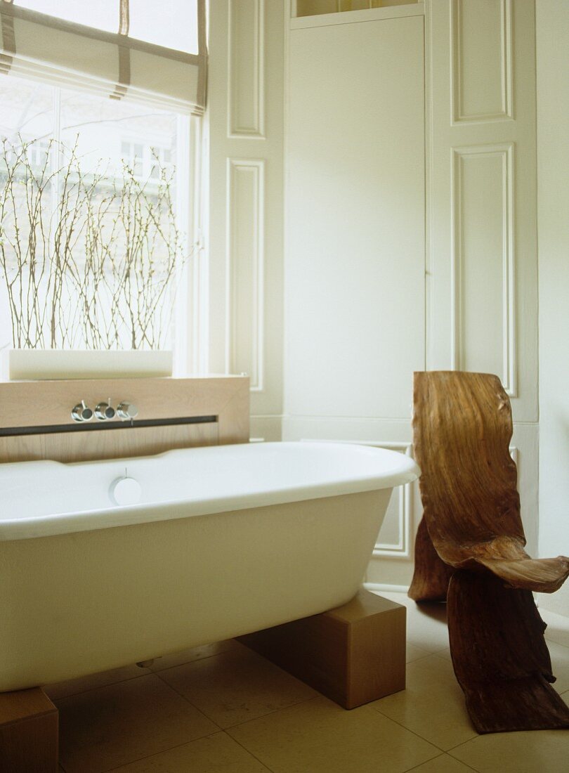 Free-standing modern bathtub supported on wooden blocks and organic, gnarled wood chair