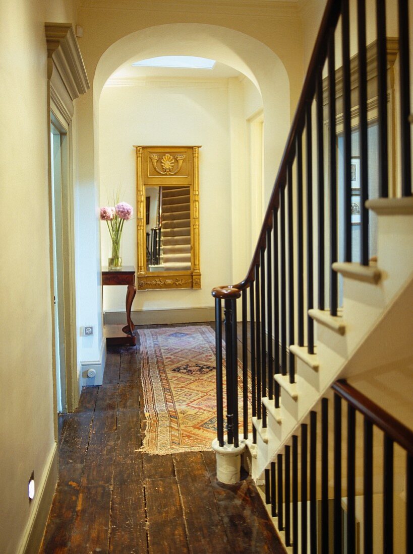 Traditional hall and staircase in period setting with elaborate, gold-framed mirror and antique console table