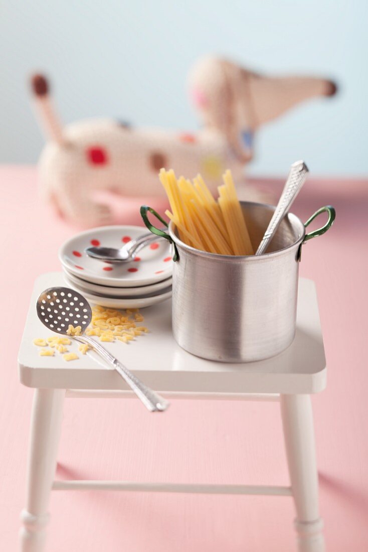 Saucepan with pasta and plates on white stool