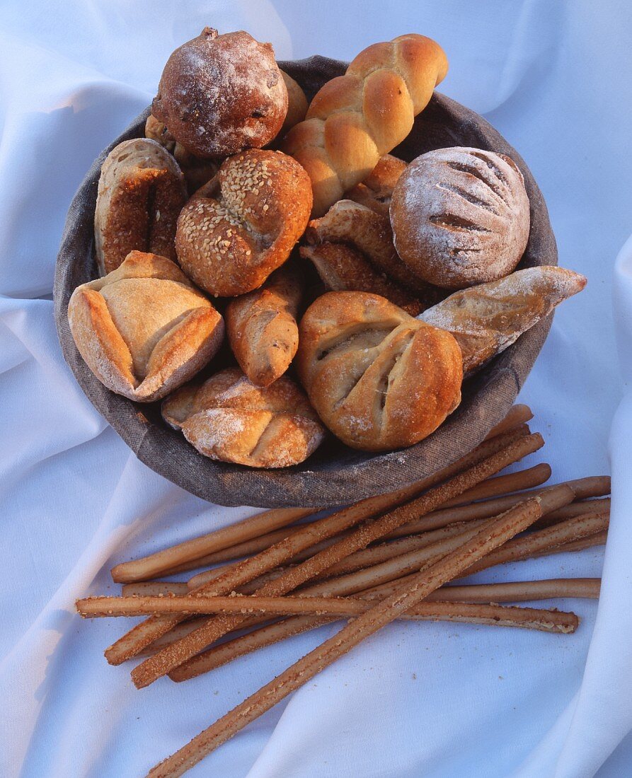 Assorted rolls in a basket; with bread sticks next to it