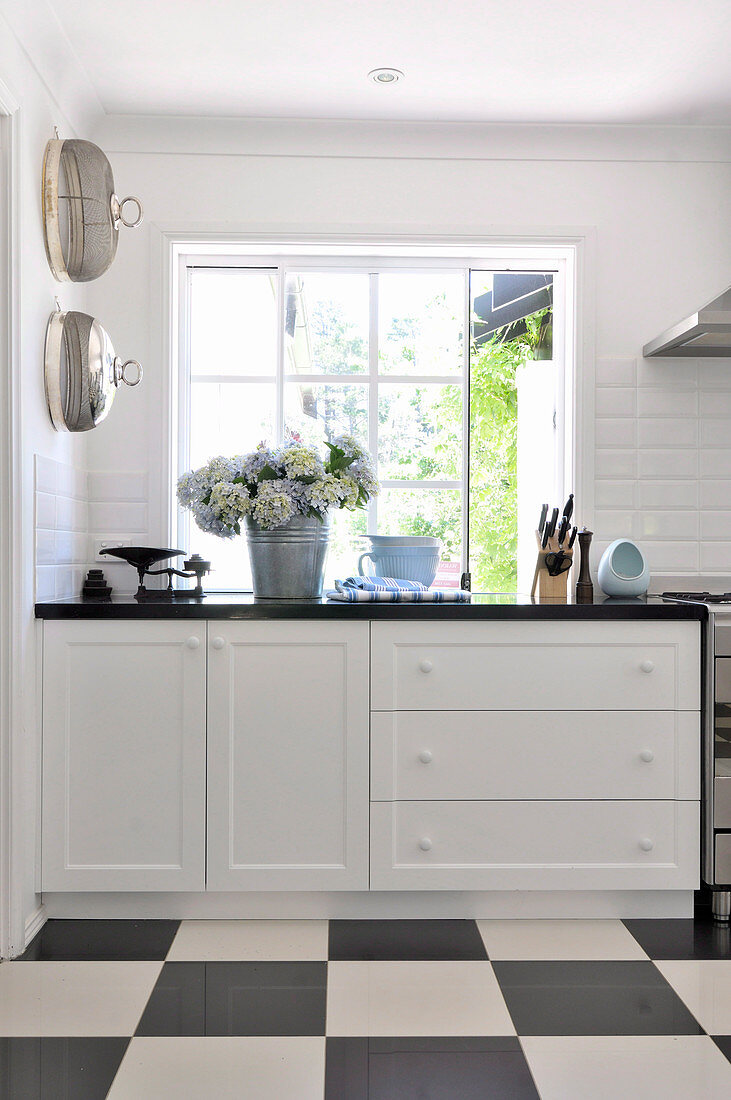 Kitchen counter below window and black and white chequered floor in country kitchen