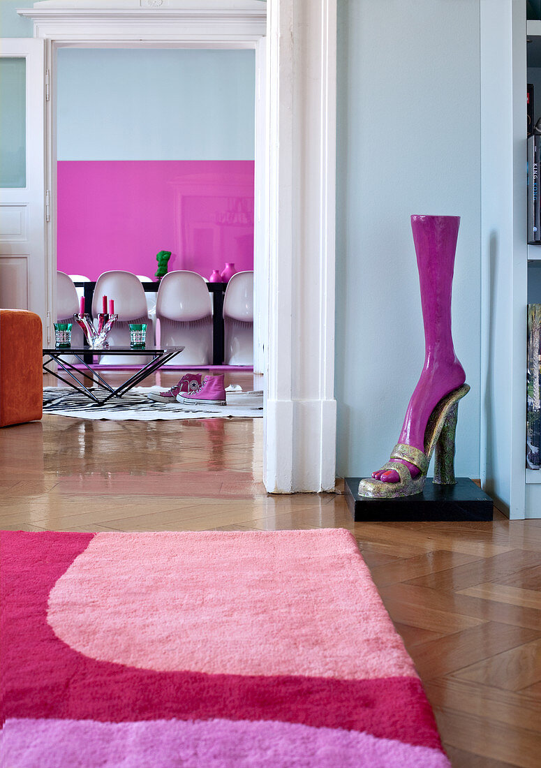 Detail of rug in shades of pink and lilac and shoe-shaped sculpture; dining area in background with white Panton chairs in front of pink painting