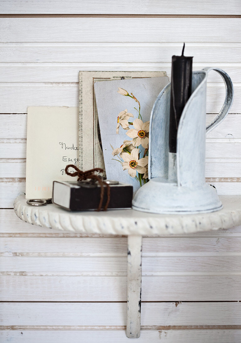 Vintage candlestick and postcard with floral motif on bracket mounted on white wooden wall