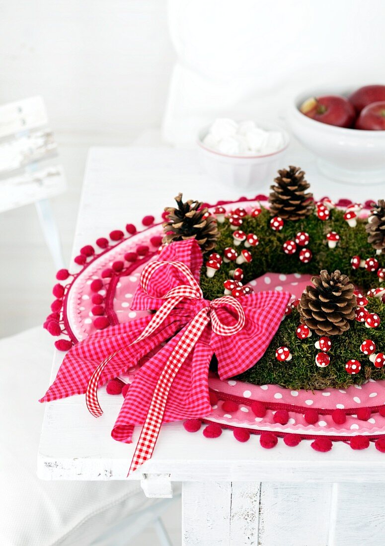 Autumnal moss wreath with pine cones and decorative mushrooms on a pink place mat