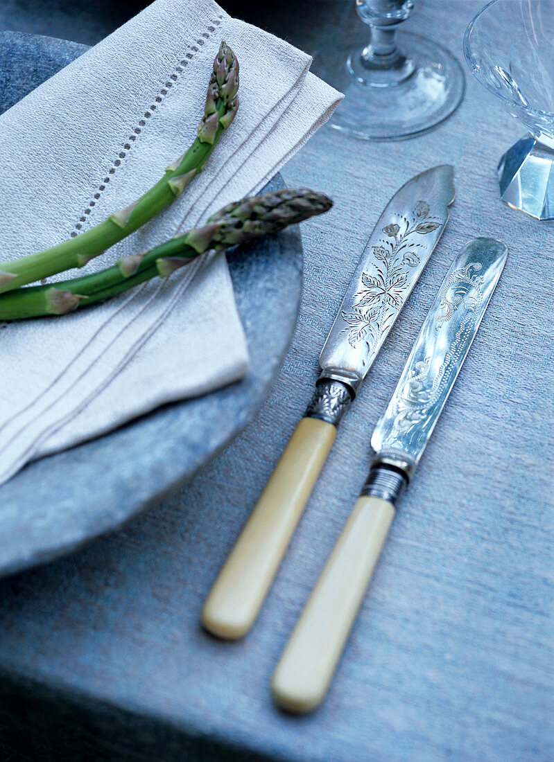 Antique knives with ivory handles next to asparagus arranged on stone plate