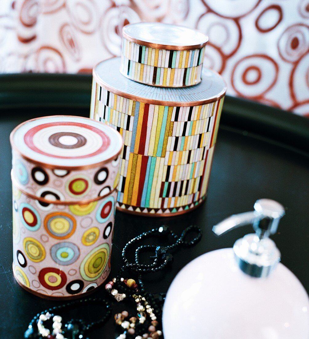 Containers with a colorful pattern next to a necklace on a black tray