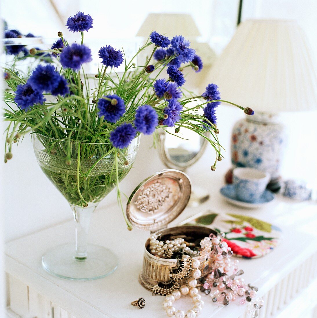 Corn flowers in a glass next to an open silver box with jewelry