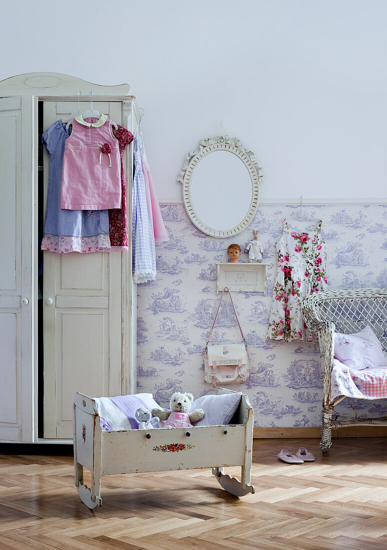 Soft toys in old dolls' cradle and white farmhouse wardrobe in rustic child's bedroom