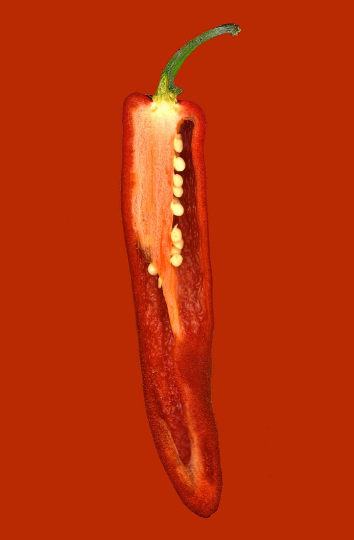 Eine halbe rote Chilischote vor rotem Hintergrund
