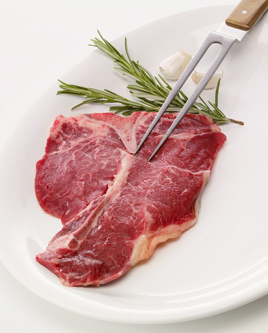 Rohes T-Bone-Steak mit Fleischgabel, Rosmarin und Knoblauch
