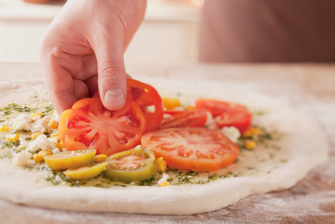 A pizza being topped with tomato slices