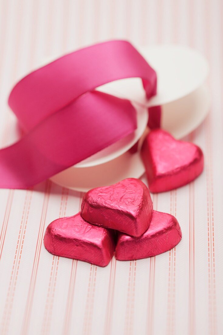Heart-shaped chocolates wrapped in red foil and a red ribbon