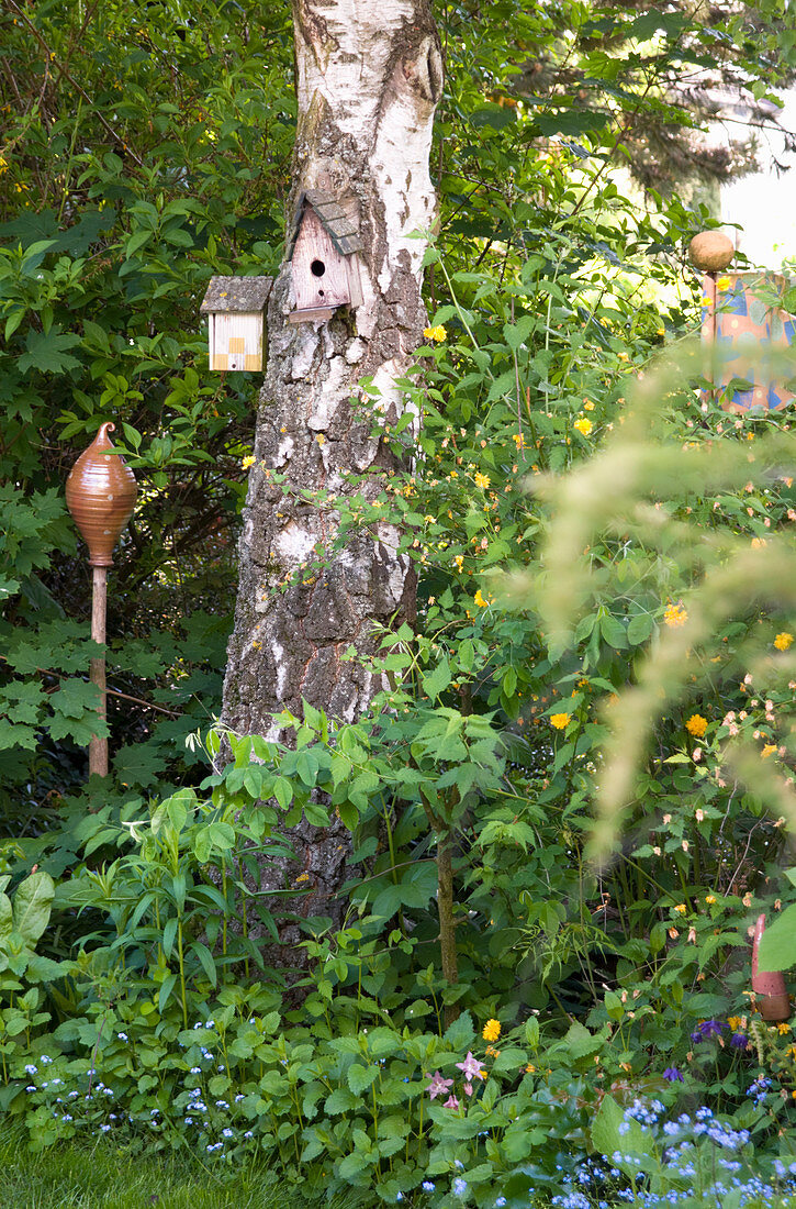 Vogelhäuschen am Baumstamm, daneben Keramikdeko