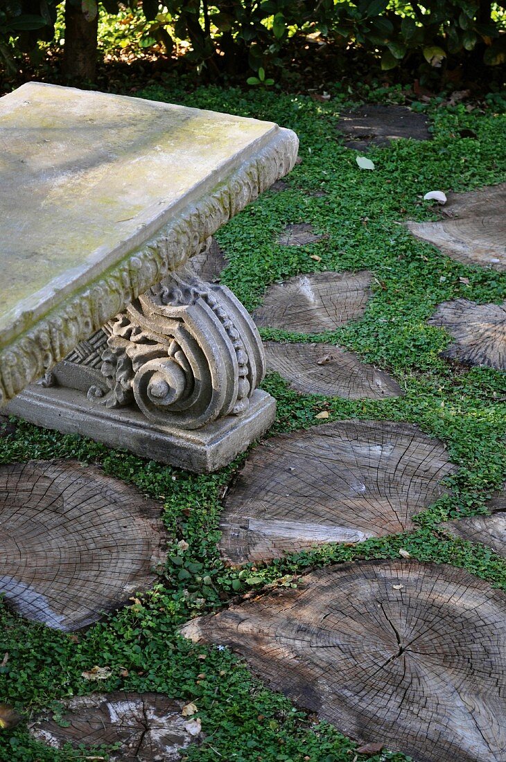 Antique stone bench in the garden and cross sections of tree trunks used as pavers