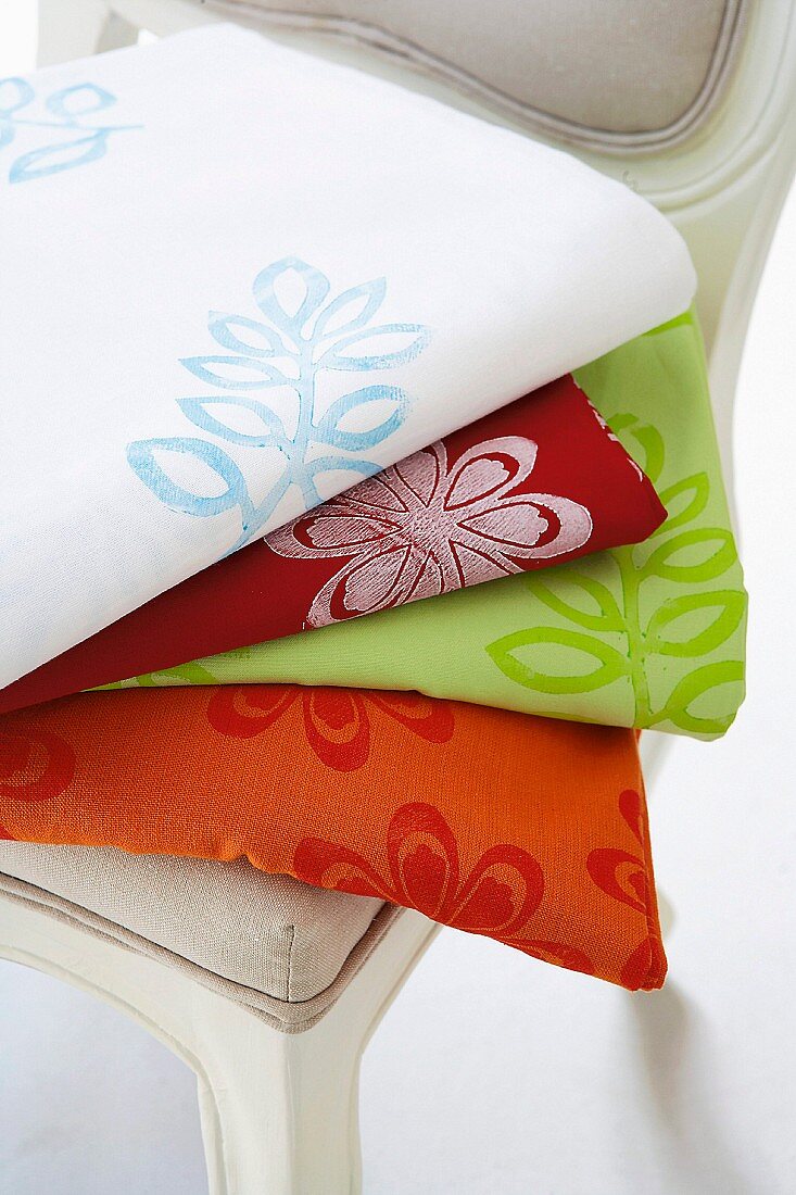 Stack of floral linocut print blankets of various colours on chair