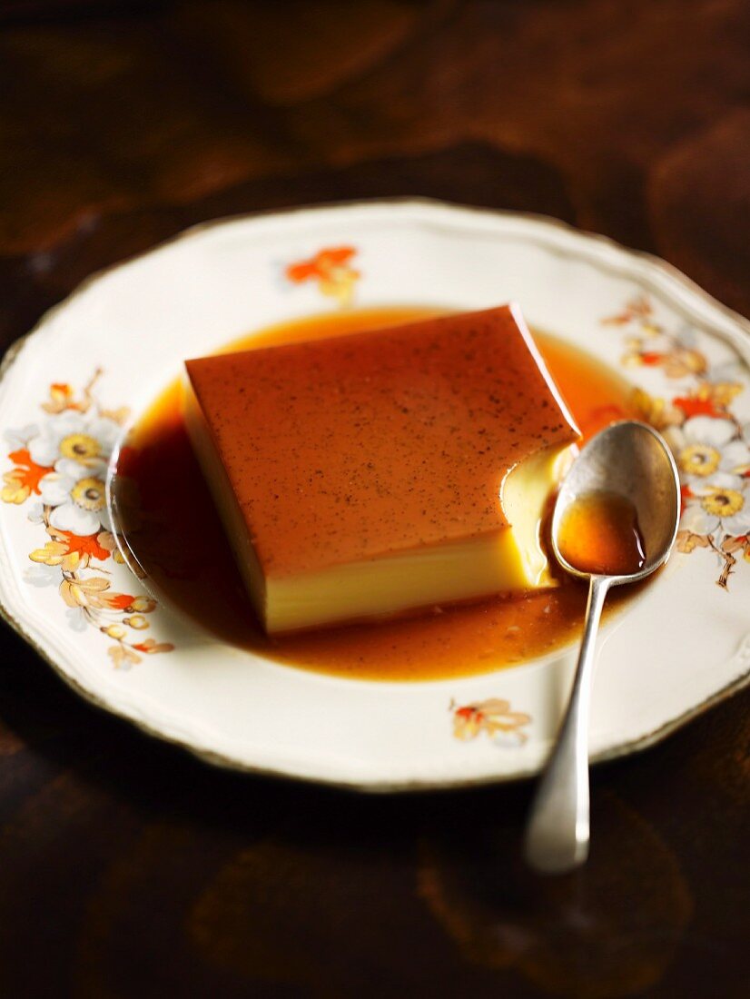 Creme caramel, with a bite out of it, on a plate with a spoon