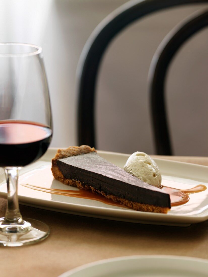 A slice of chocolate tart with caramel sauce and ice cream, and a glass of red wine