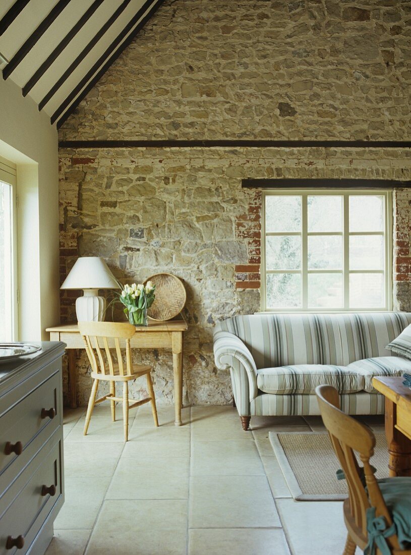 Corner of living room with rustic wooden table and sofa against stone wall