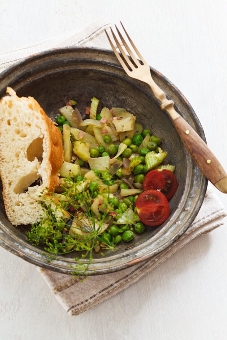 Skillet meal with fennel, cherry tomatoes, peas, bacon and baguette slice