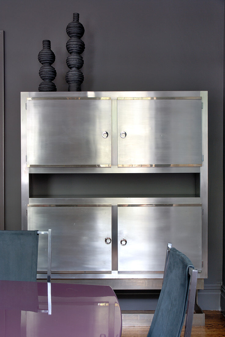 Edler Silberschrank an grauer Wand; im Vordergrund ein glänzender Esstisch und lederbezogene Esszimmerstühle