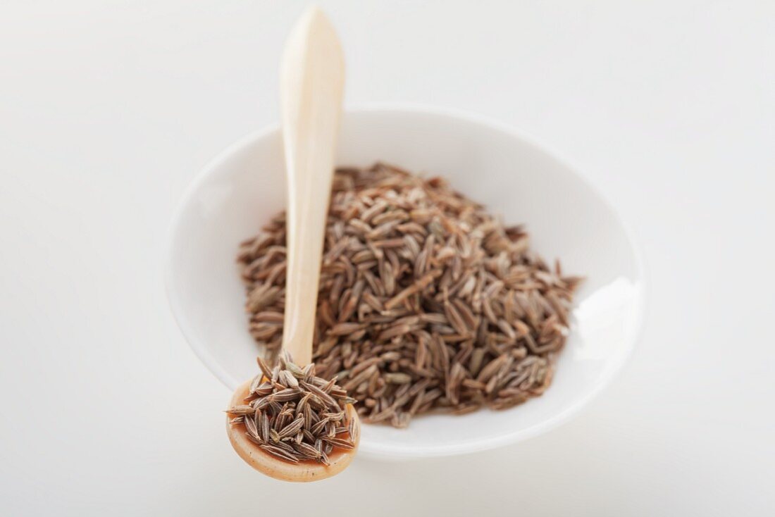 Cumin seed in a small bowl and on wooden spoon