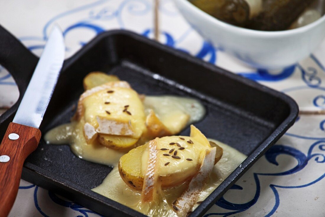 Potatoes topped with grilled cheese in a raclette pan