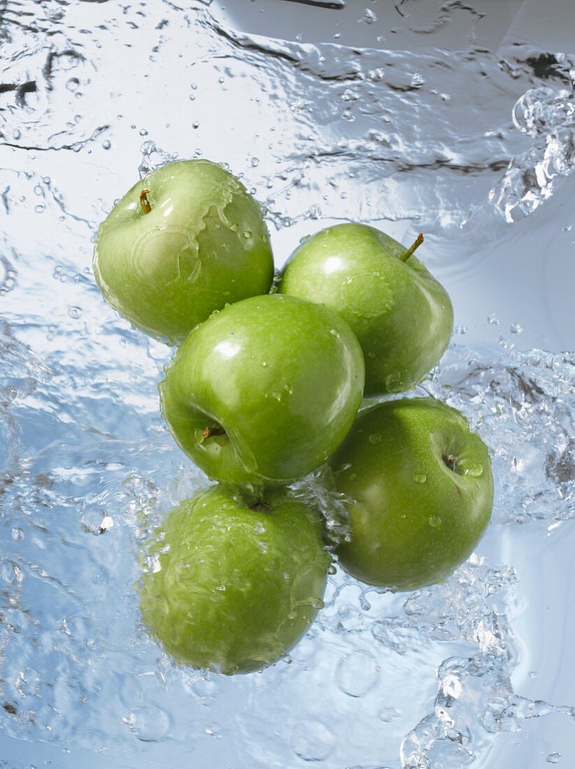Five Granny Smith apples dropping into water