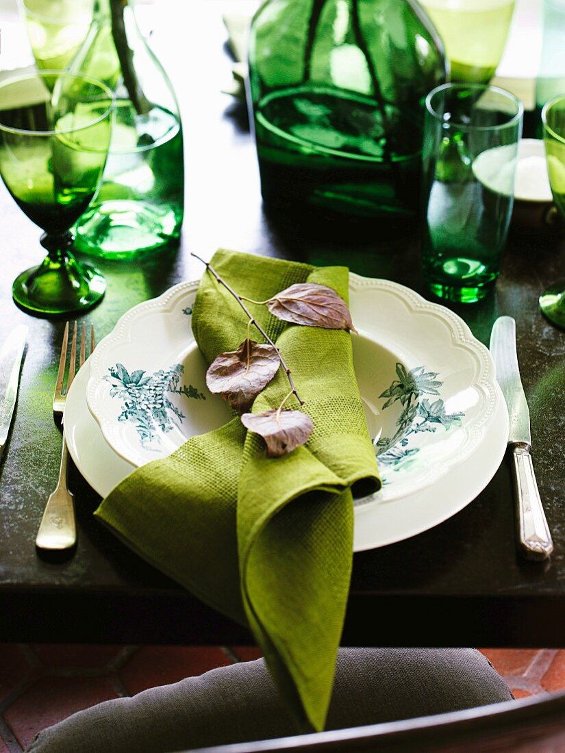 A place setting on a table laid with green glasses, bottle and napkins