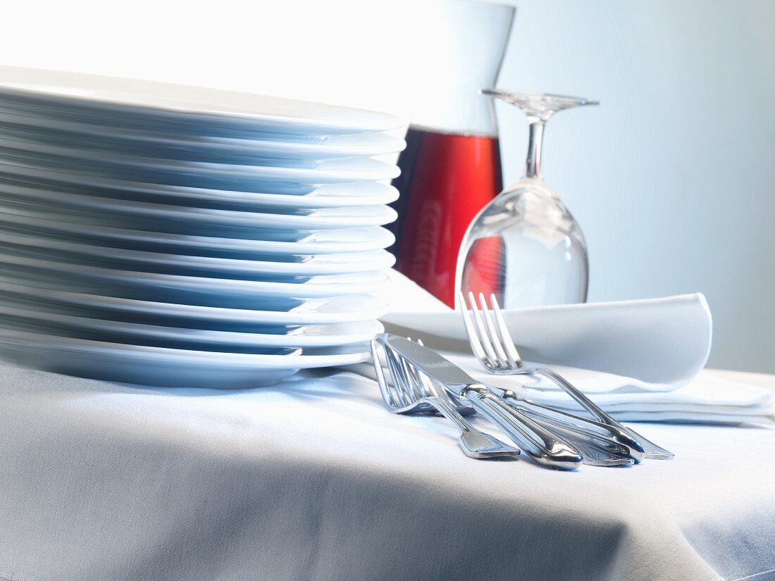 Gestapelte Porzellanteller auf Tisch mit Stoffservietten, Besteck und Gläsern