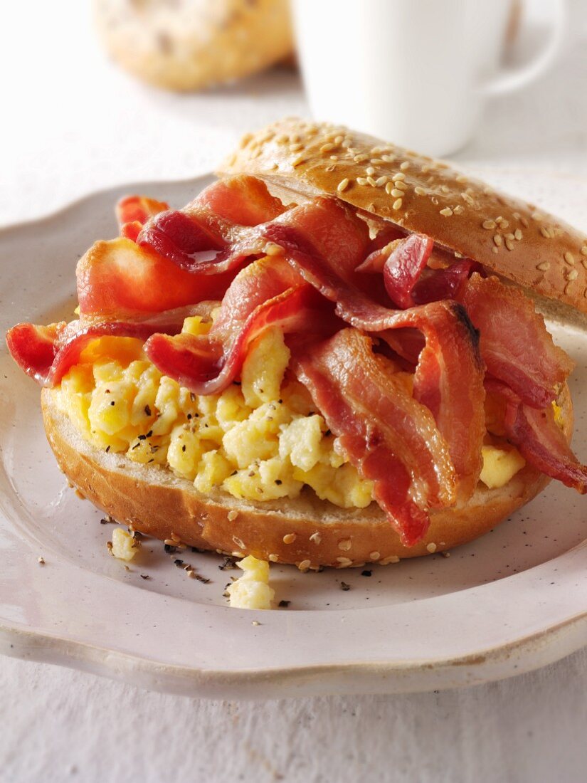 A bagel topped with scrambled eggs and crispy bacon