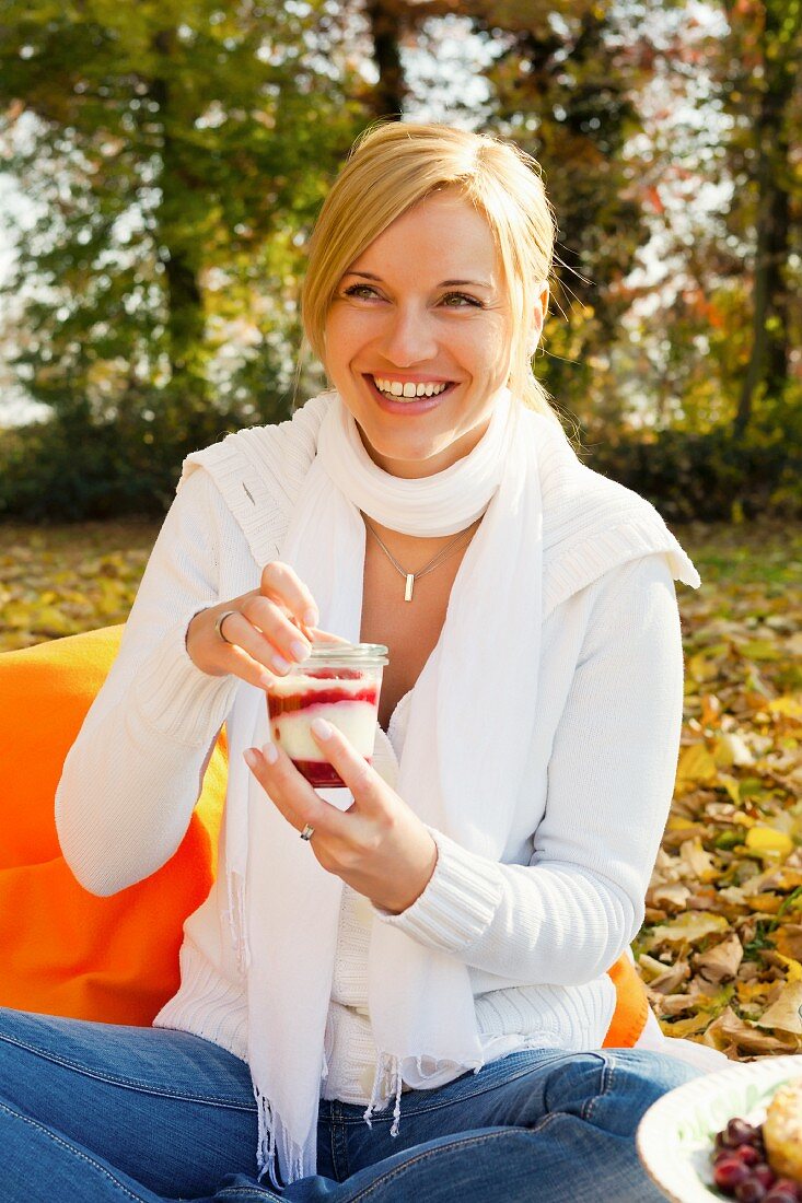 Frau isst Joghurtdessert beim herbstlichen Picknick