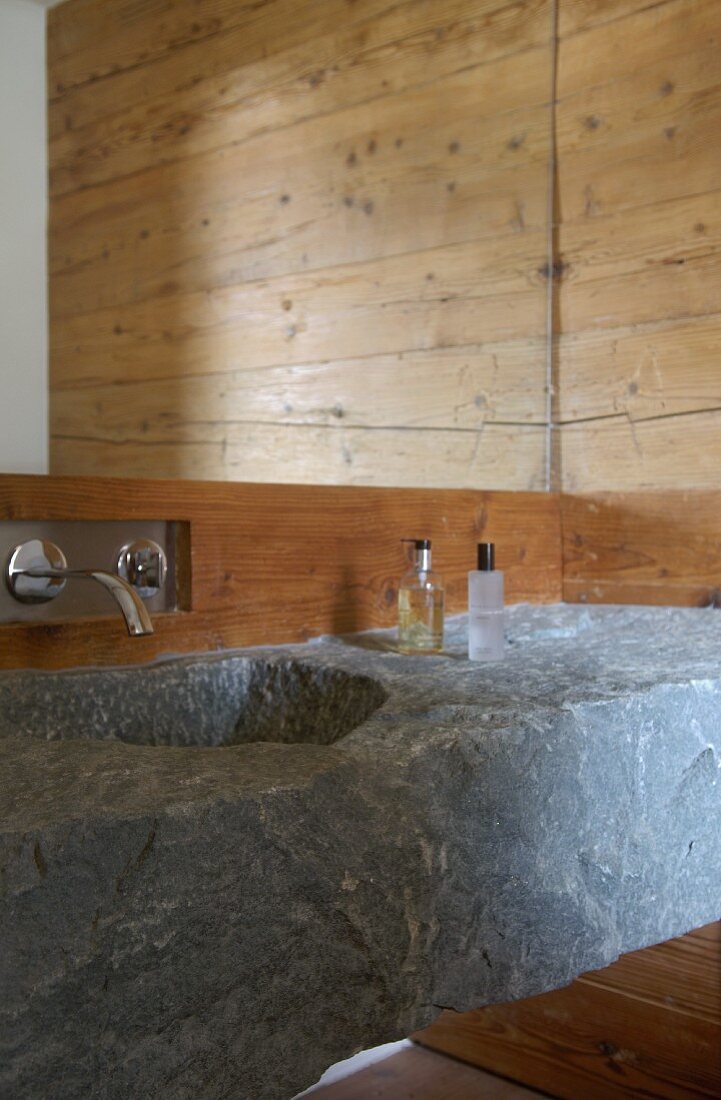 Wash basin hollowed out of stone block below designer wall-mounted tap and mirror
