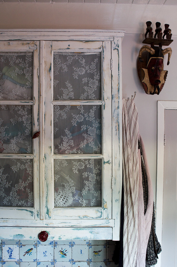 A vintage cabinet with voile curtains instead of glass above Delft tiles in a bathroom