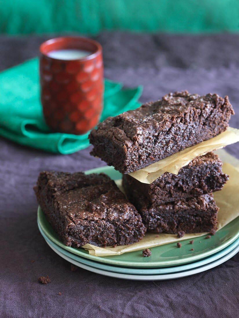 Dark Chocolate Gluten Free Brownies Stacked on Stacked Plates; Glass of Milk