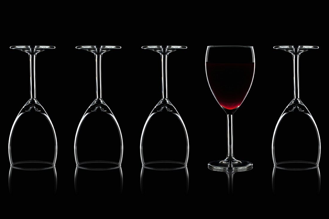 Row of wine glasses and a glass of red wine against a black background