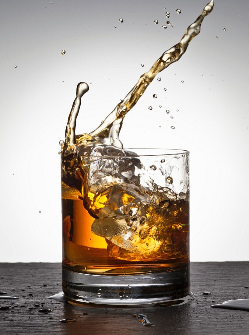 Eiswürfel fällt in Whiskeyglas