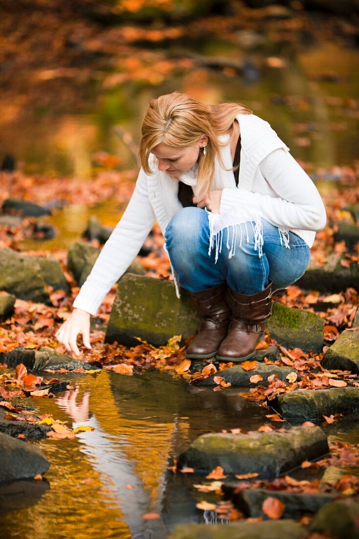 Frau an einem Bach im herbstlichen Wald