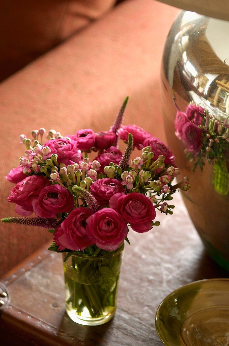 A bouquet of ranunculus reflected in a silver vase