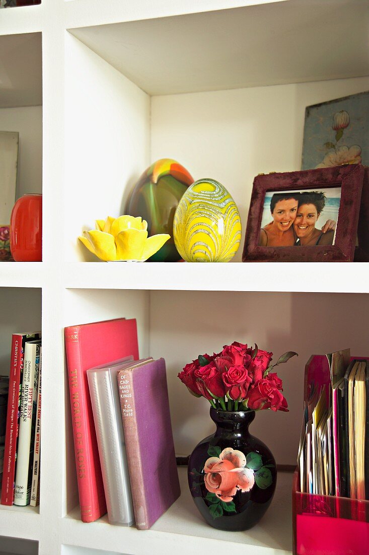 White book shelves with vase of roses, yellow glass eggs and framed family photos