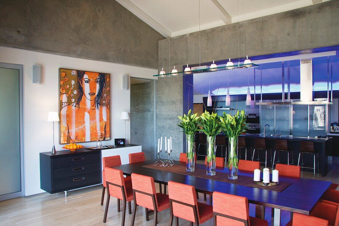 Ex[posed concrete around a modern dining area in front of a designer kitchen illuminated with blue light with a long counter