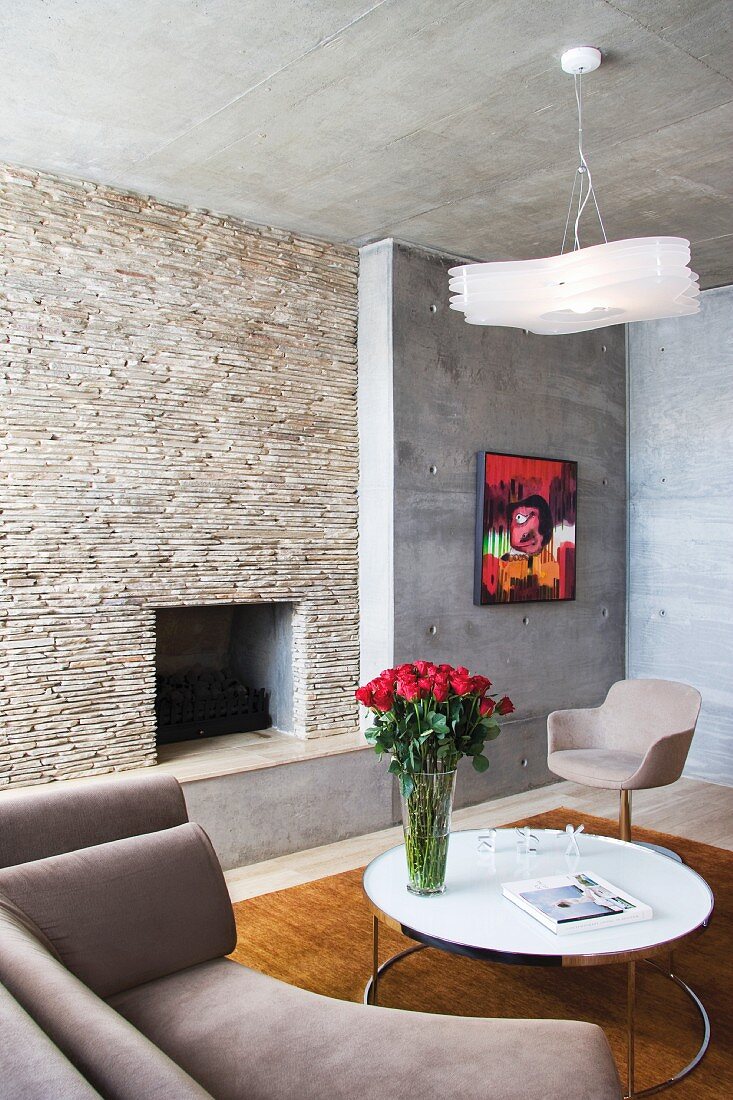 Corner sitting with designer furniture in front of a fireplace clad in natural stone and raw exposed concrete walls