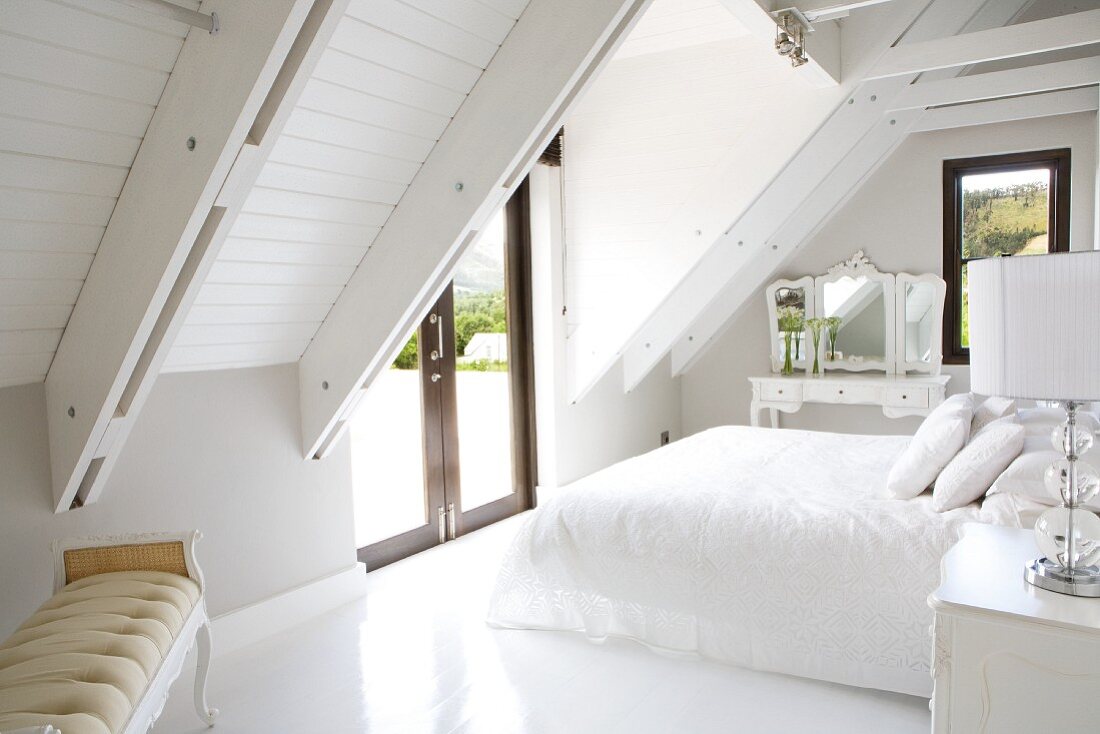 Elegant, antique-style furniture in white bedroom under exposed roof structure of modern country house