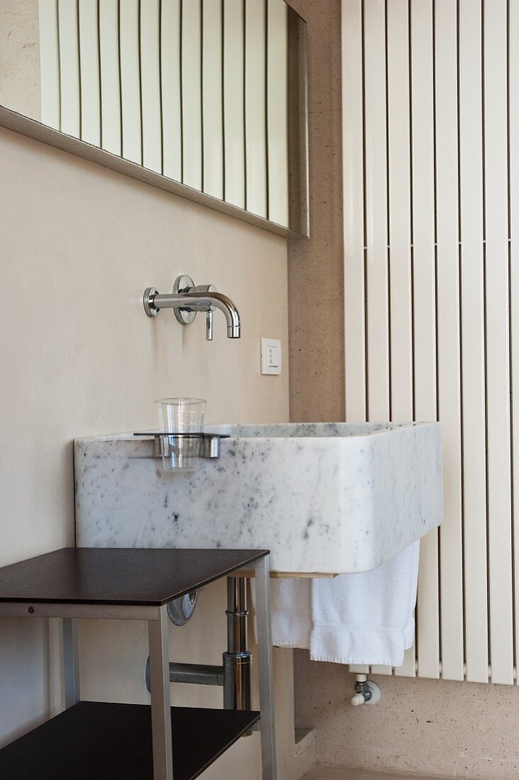 Modern stone sink with wall-mounted taps and side table in corner of bathroom