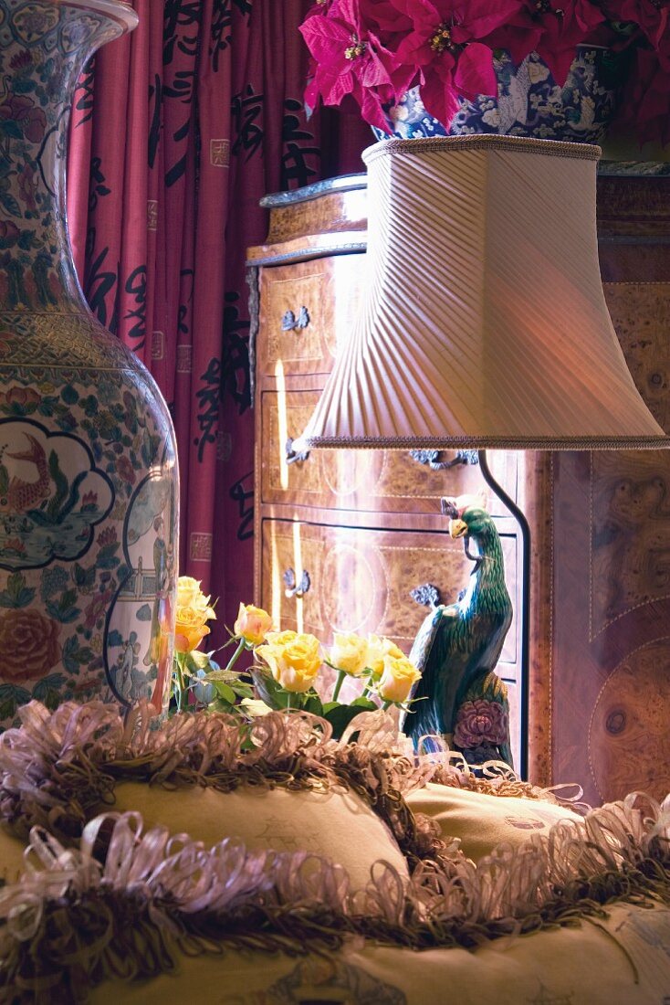 Boudoirausschnitt mit Stehlampe neben bunter Papageienfigur und Barockkommode